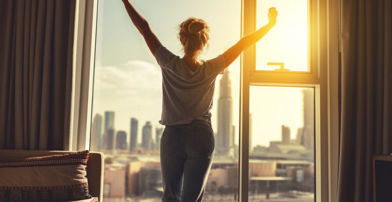 happy woman stretches and opens curtains at window in morning happy woman stretches and opens curtains at window in morning